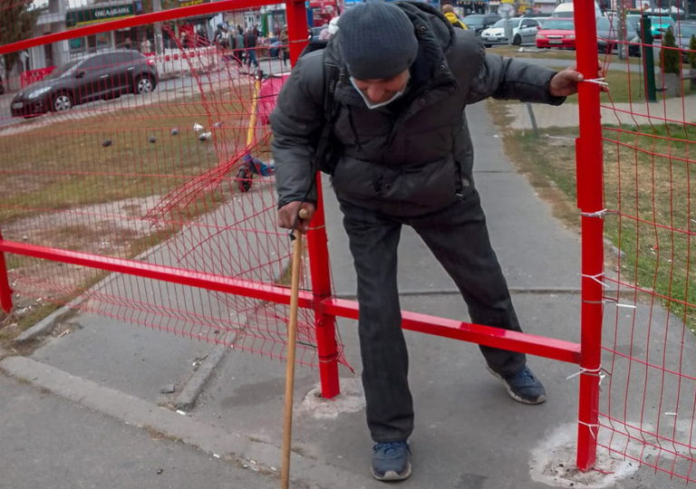 На Оболони на тротуаре возле метро поставили забор, но местные жители пробили дыру и пролазят сквозь нее